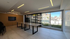 A modern, spacious room with a long table, a flat-screen TV mounted on the wall, and large windows offering a city view. - Apartment in Nuñez (Buenos Aires)