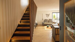 Een modern interieur met een houten trap, een zithoek met een bank en salontafel, en een aan de muur bevestigd kunstwerk.