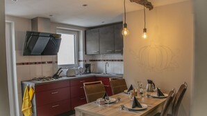 Una cocina moderna con armarios rojos, una mesa de comedor preparada para cuatro personas y un amplio ventanal que proporciona luz natural.