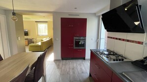 Una cocina compacta con un armario rojo, una estufa a gas y un microondas. En la zona de estar contigua, hay una mesa de comedor con sillas y un sofá amarillo.