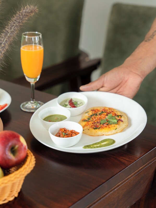A dining table with a plate of food, a glass of orange juice, and a basket of fruit. - Vanthra Vilas (Bali)