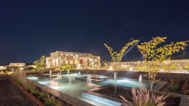 A swimming pool with multiple water features, surrounded by landscaped areas and a building in the background. - Vanthra Vilas (Bali)