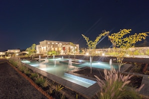 A swimming pool with multiple water features, surrounded by landscaped areas and a building in the background. - Vanthra Vilas (Bali)