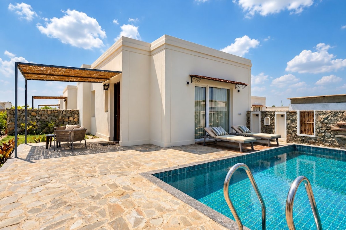 A modern outdoor pool area with stone flooring, lounge chairs, and a covered seating area.