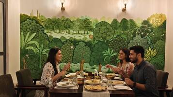 A dining area with a mural of a forest scene, a table set with plates and glasses, and two wall-mounted lamps.