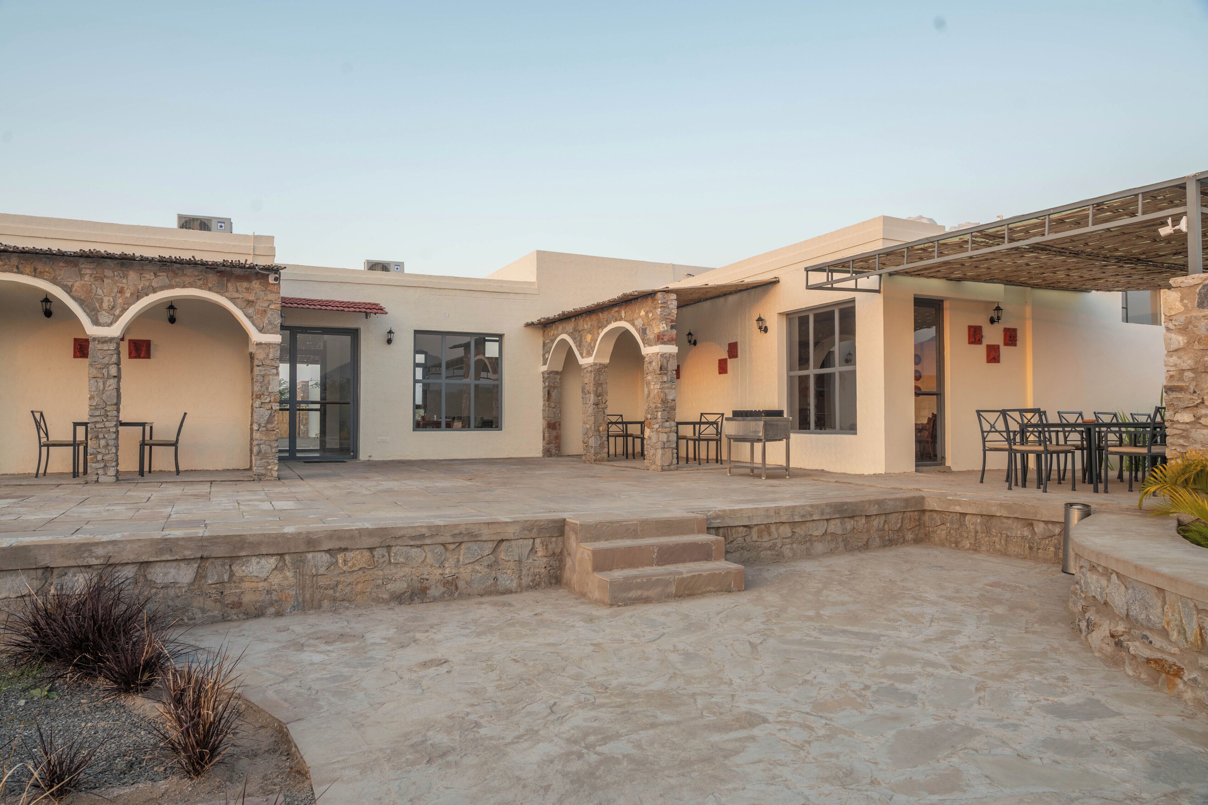 Un patio con escalones de piedra, mobiliario exterior y una zona cubierta con mesas y sillas.