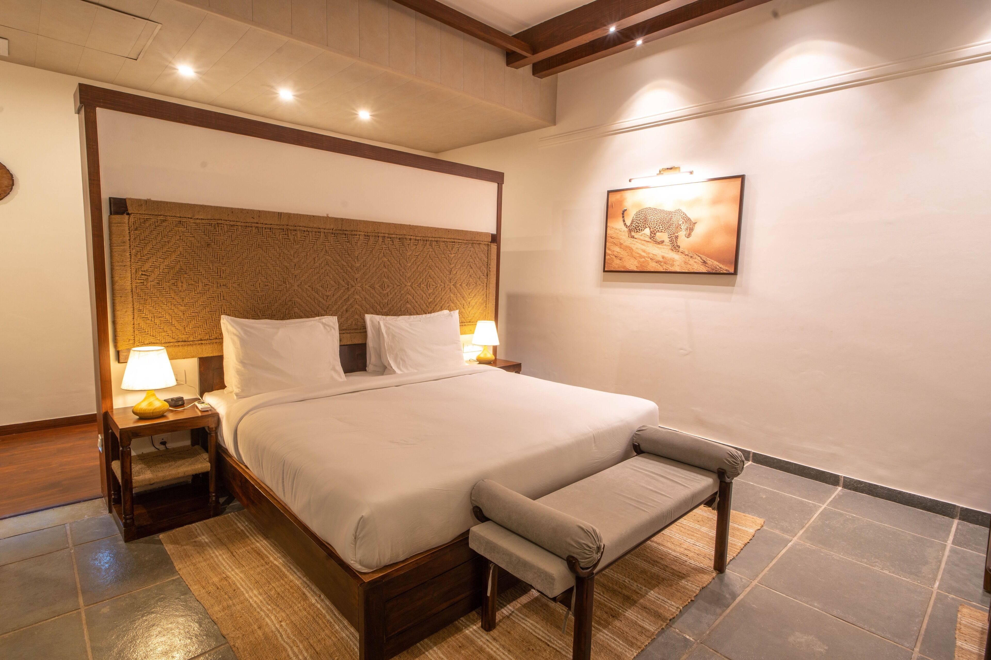 Una cama bien hecha con cabecera de madera, una lámpara de noche y un banco.