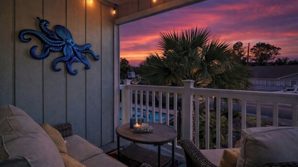 Un espace extérieur abrité avec des sièges, offrant une vue sur le coucher du soleil, un décor mural représentant un poulpe et une petite table avec une bougie.