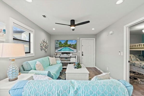 A modern living room with a ceiling fan, a TV, a sofa, and a coffee table. - Dog Friendly 2BR/2BA- Pool- Summer Times #1 (North Myrtle Beach)