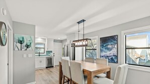 Une cuisine moderne avec des meubles blancs, une table à manger en bois et un luminaire suspendu.