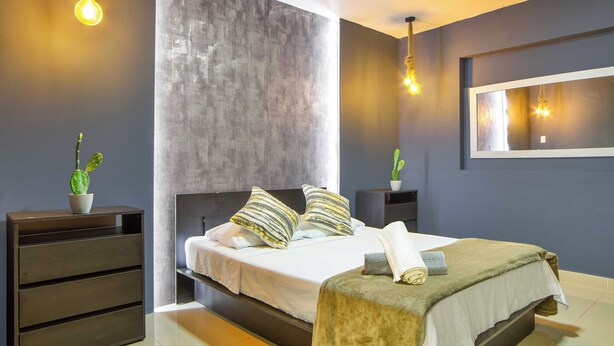 A modern bedroom with a large bed, bedside tables, a mirror, and hanging light fixtures. - 5BR by Lleras Park w Arcade & Foosball (Medellin)