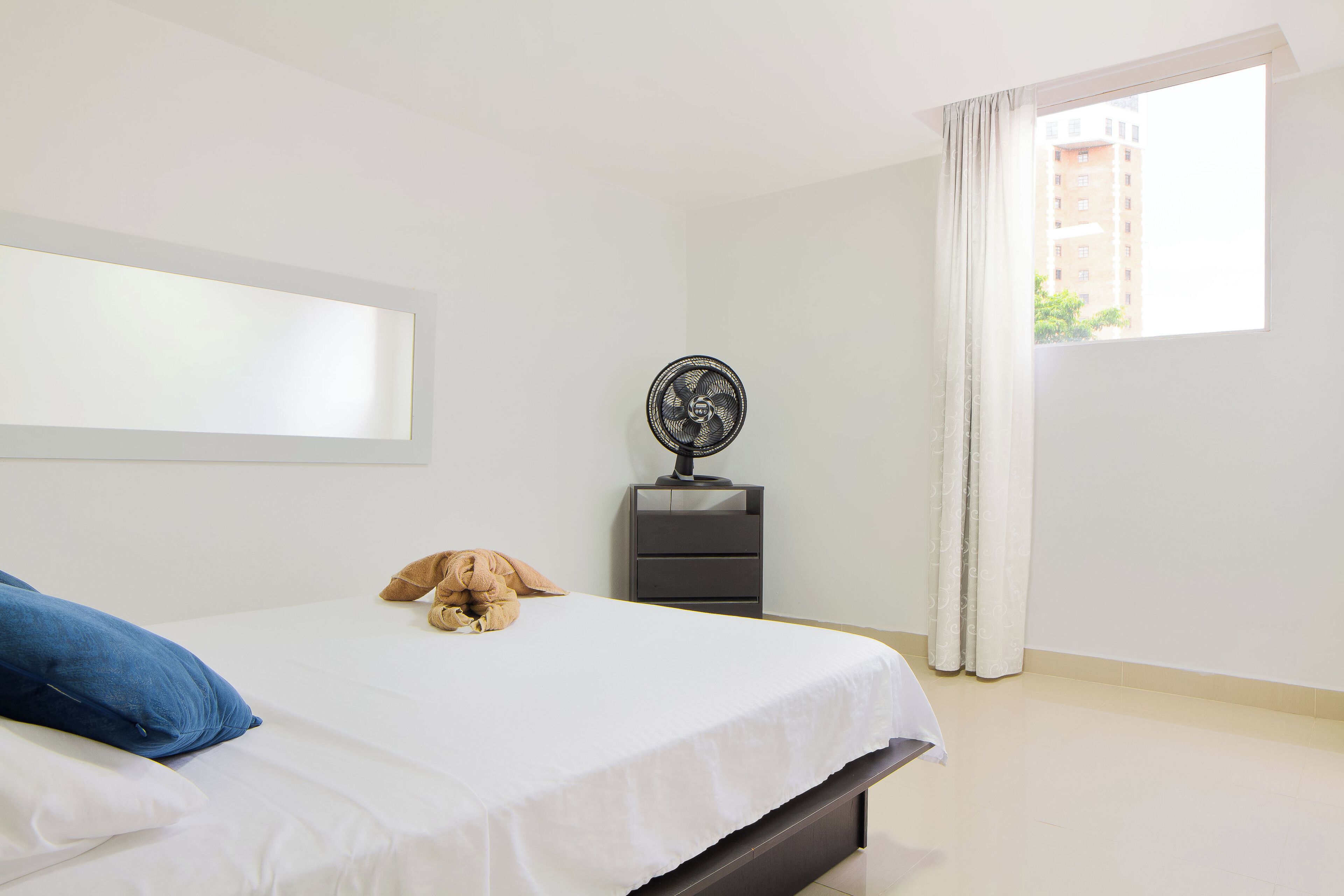Une chambre à coucher avec un lit, une table de chevet, un ventilateur et une fenêtre avec des rideaux.