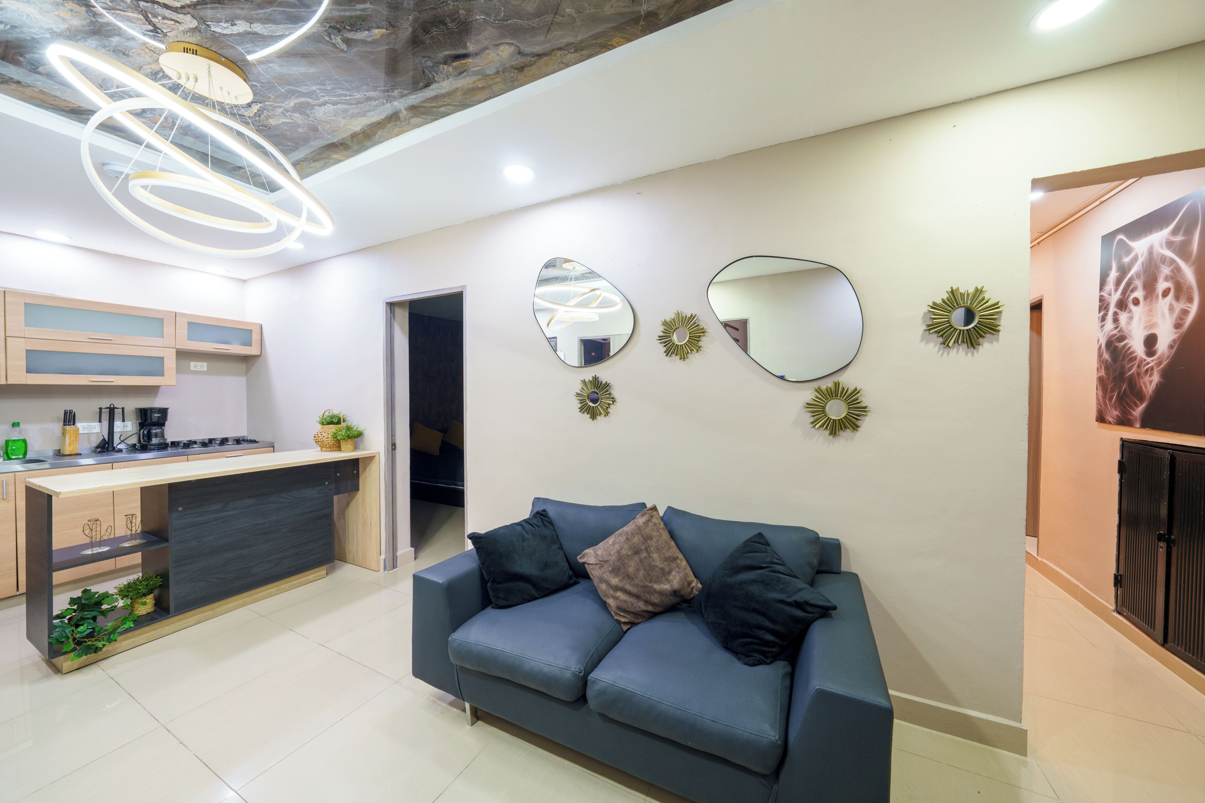 A modern living room with a blue sofa, a kitchen area, and decorative mirrors on the wall.