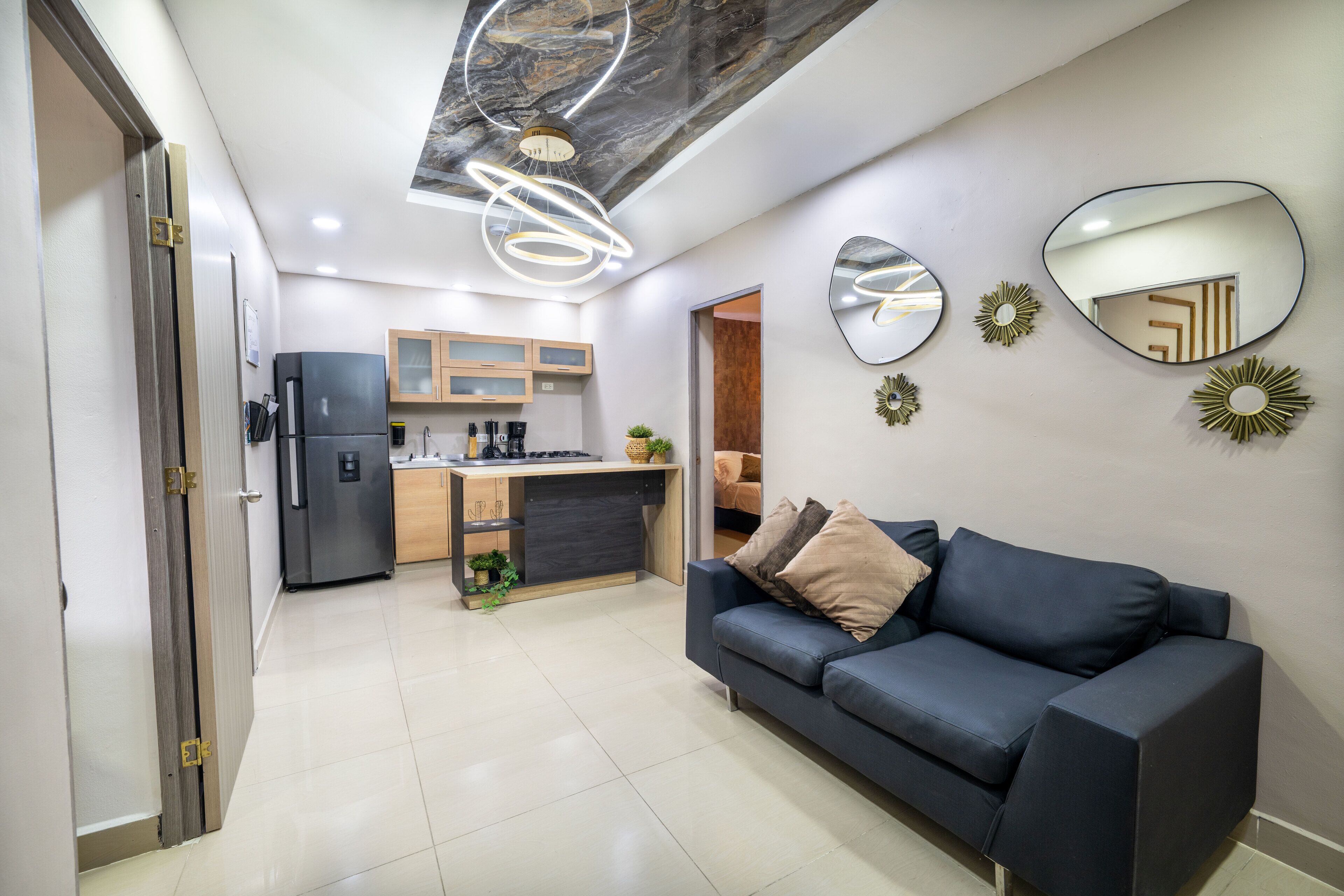 A modern living room with a dark blue sofa, a kitchen in the background, and decorative mirrors on the wall.