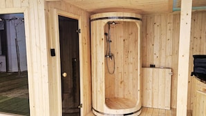 A wooden sauna with a curved design, a showerhead, and a small shelf with bottles. - Holiday Cottages, Sauna and hot tub Included (Mielno)