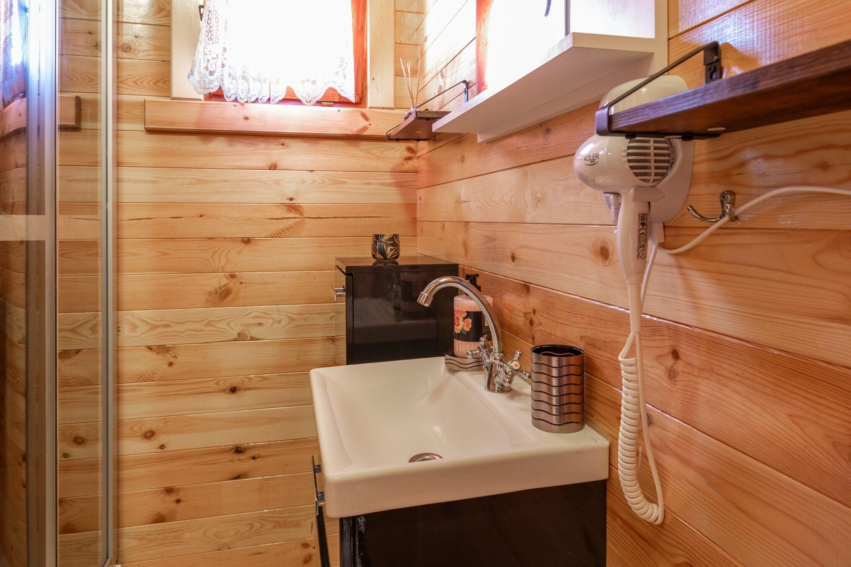 A wooden cabin bathroom with a white sink, a hairdryer, and a small black appliance.