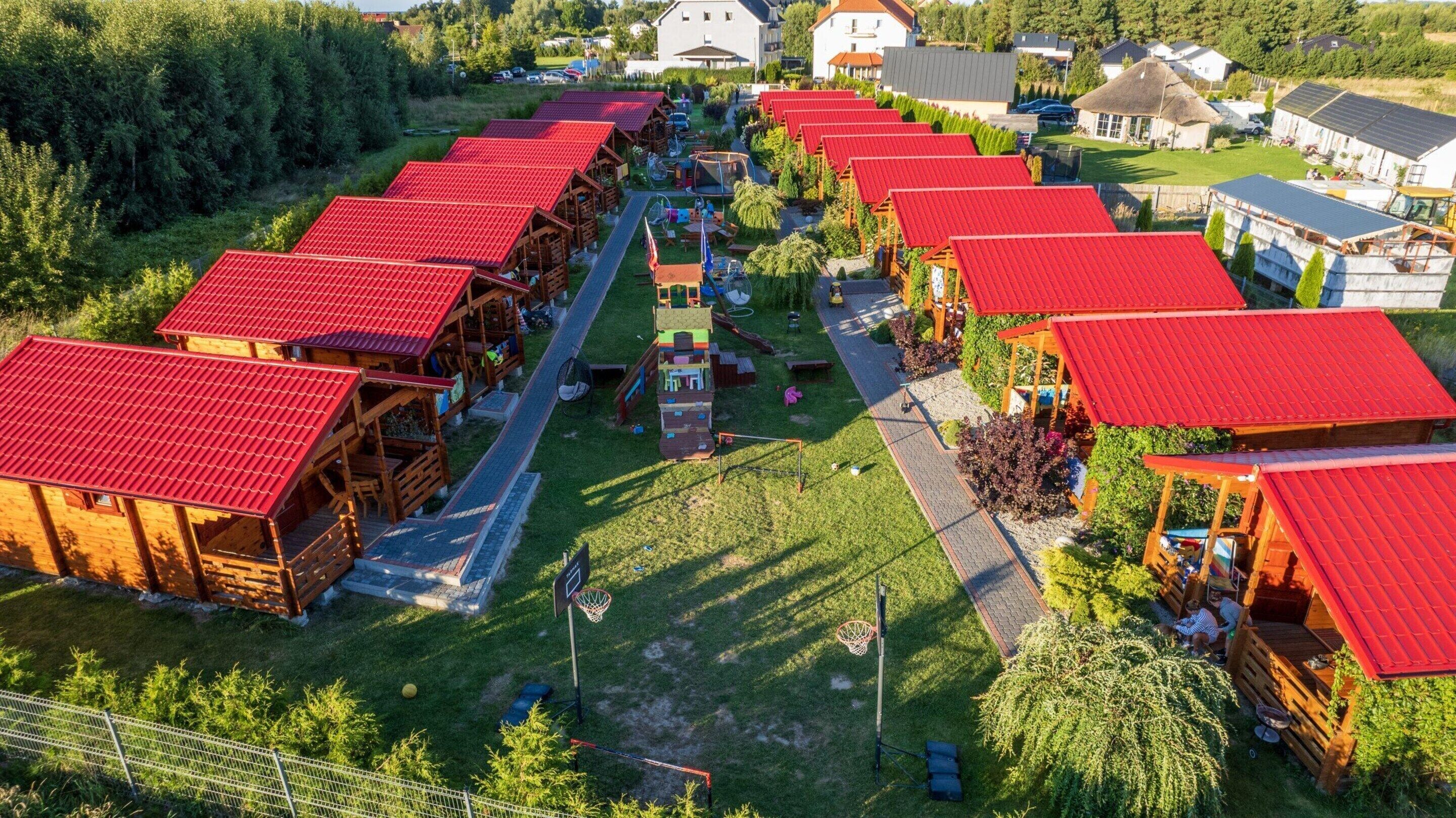 A row of log cabins with red roofs, arranged in a linear fashion with a central pathway.