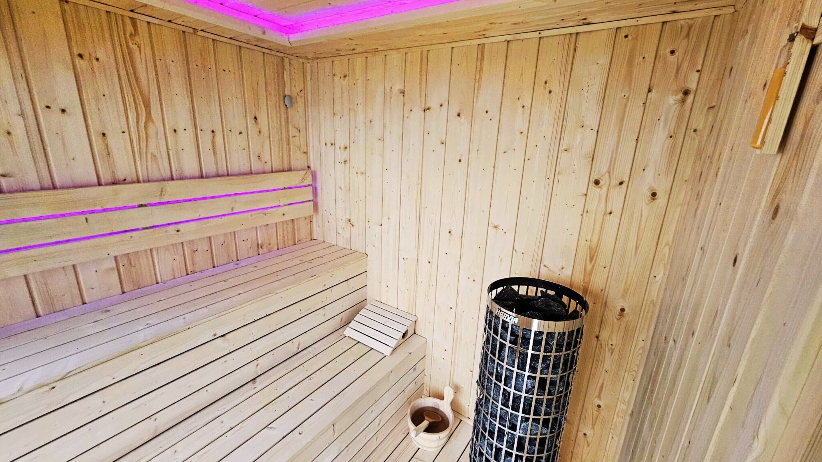 Un sauna en bois avec un banc, un récipient en métal et un seau en bois.
