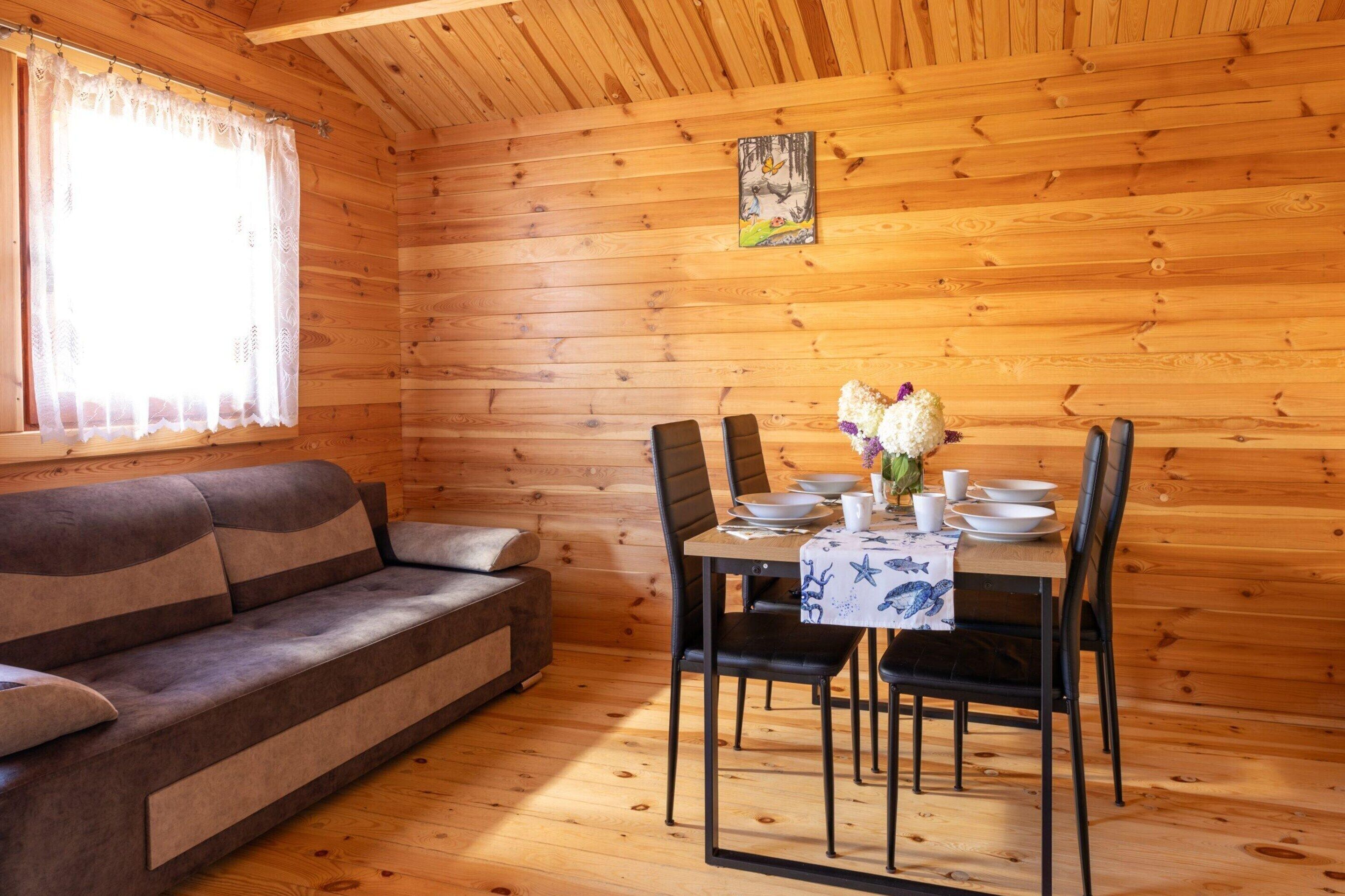 Interior de uma cabana de madeira com sofá, mesa de jantar, cadeiras e um quadro na parede.
