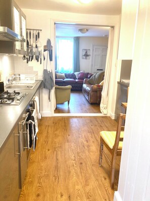 A compact kitchen with modern appliances, a dining area with a wooden table, and a cozy living room with a sofa and curtains. - Garden & Parking within the Old City Walls. (Canterbury)