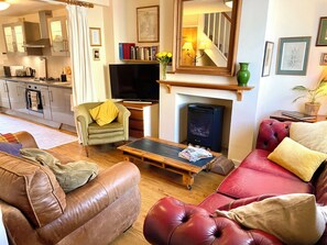 A living room with a sofa, armchair, coffee table, fireplace, television, and kitchen area. - Garden & Parking within the Old City Walls. (Canterbury)