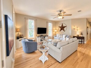 Un salon avec un canapé, une table basse, un téléviseur et un ventilateur de plafond.