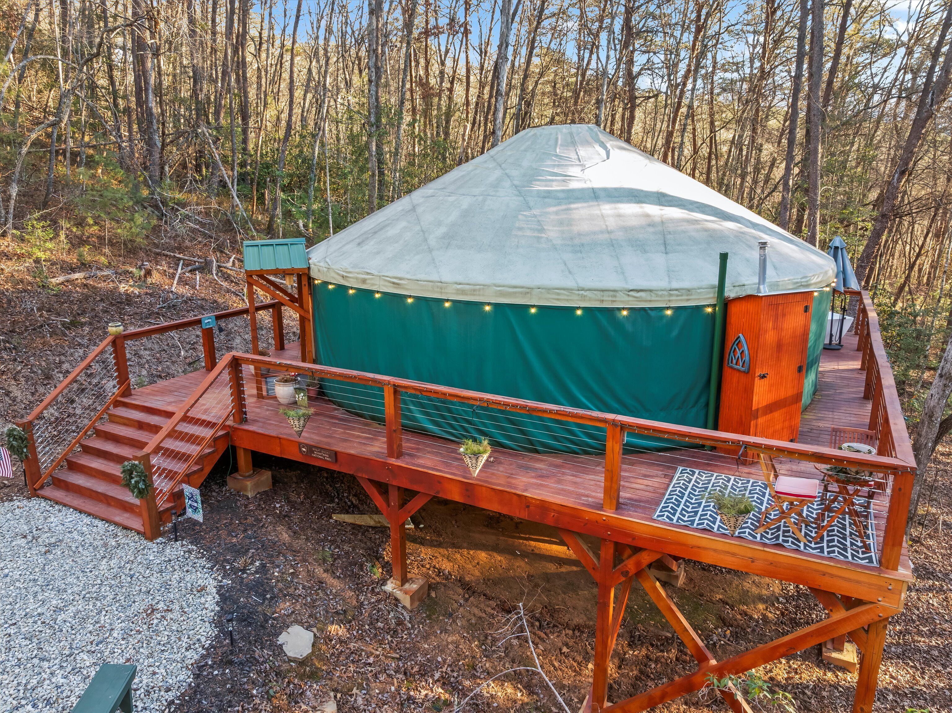 A yurt with a wooden deck and a covered entrance, surrounded by trees.