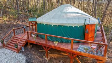 A yurt with a wooden deck and a covered entrance, surrounded by trees.