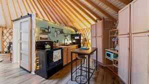 Une cuisine compacte avec des meubles en bois, une cuisinière noire et un petit coin repas équipé d’un tabouret.