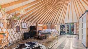 L’intérieur chaleureux d’une yourte, avec un canapé, une table basse en bois, un tapis en peau de vache et un téléviseur.