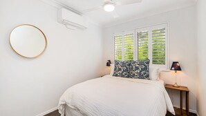 Una camera da letto con un letto, uno specchio tondo, una ventola a soffitto e una finestra con persiane.