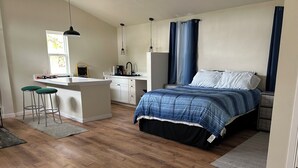 A bedroom with a bed, a desk, two stools, and a kitchenette. - Welcome to the Savanna Shire! Cozy one room cabin for a lovers getaway! (Thomson)