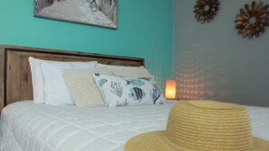 Un lit recouvert d’une couette blanche, avec un chapeau de paille posé dessus.