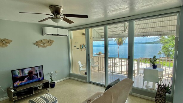 Un salon équipé d’un téléviseur, d’un ventilateur de plafond et d’une porte-fenêtre coulissante donnant sur un balcon avec vue sur la mer.