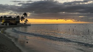 Une plage au coucher du soleil, avec des palmiers et un bâtiment doté d’un balcon.