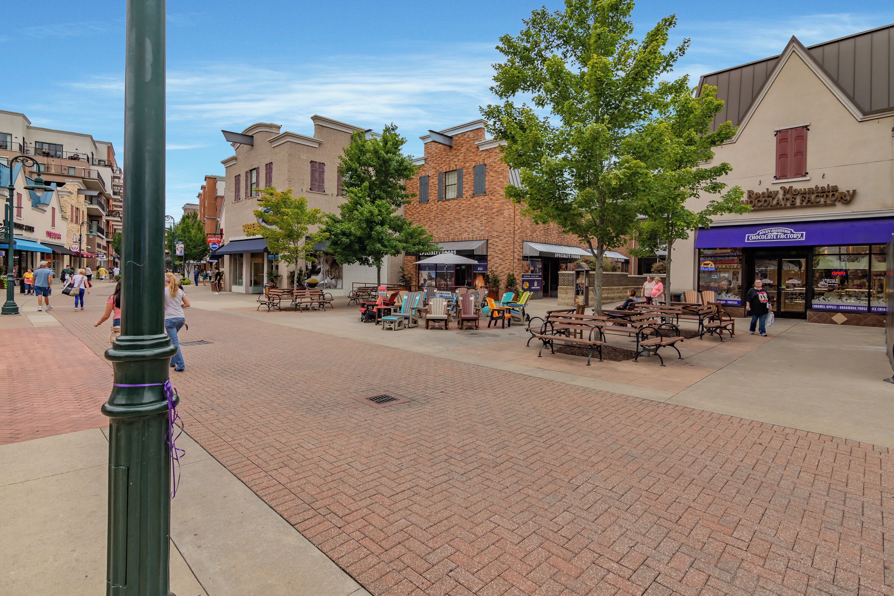 A public square with outdoor seating, brick pavement, and various shops.