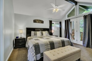 A bedroom with a large bed, a nightstand, a lamp, a ceiling fan, and a window with curtains. - Eagles Landing (Branson)