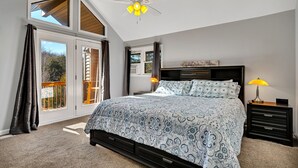 Quarto com cama grande, ventilador de teto, mesa de cabeceira e vista para o exterior.