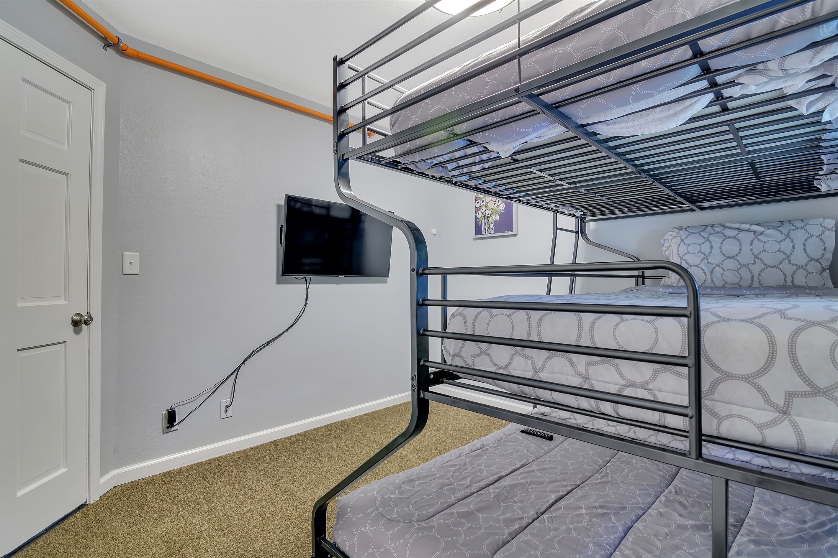 A bunk bed room with a TV mounted on the wall, a door, and a carpeted floor.