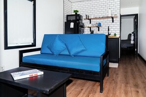 Un soggiorno moderno con un divano blu, un tavolino da caffè nero, un mobile TV nero e un angolo cottura con un forno a microonde e un armadietto nero.