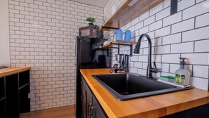 Eine moderne Küche mit einem schwarzen Spülbecken, einer Holz Arbeitsplatte und einem schwarzen Kühlschrank. Über dem Spülbecken befindet sich ein Regal mit einer Pflanze und Küchenutensilien.