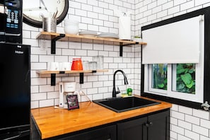 A kitchen with a black refrigerator, a coffee maker, a sink, and a window with greenery outside. - Top-Floor Corner Beachfront Suite with Reef Views | Aqua Vista – Suite 6 (San Pedro)