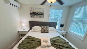 Un letto ben rifatto con una coperta verde, un quadro appeso al muro e una ventola a soffitto.