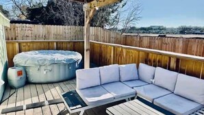 Un patio esterno coperto con una vasca idromassaggio, un divano angolare bianco e un tavolino.