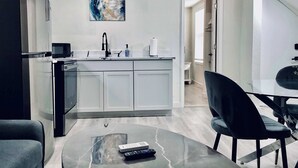 Una cucina moderna con isola centrale, zona pranzo con tavolo in vetro e soggiorno con divano e tavolino.