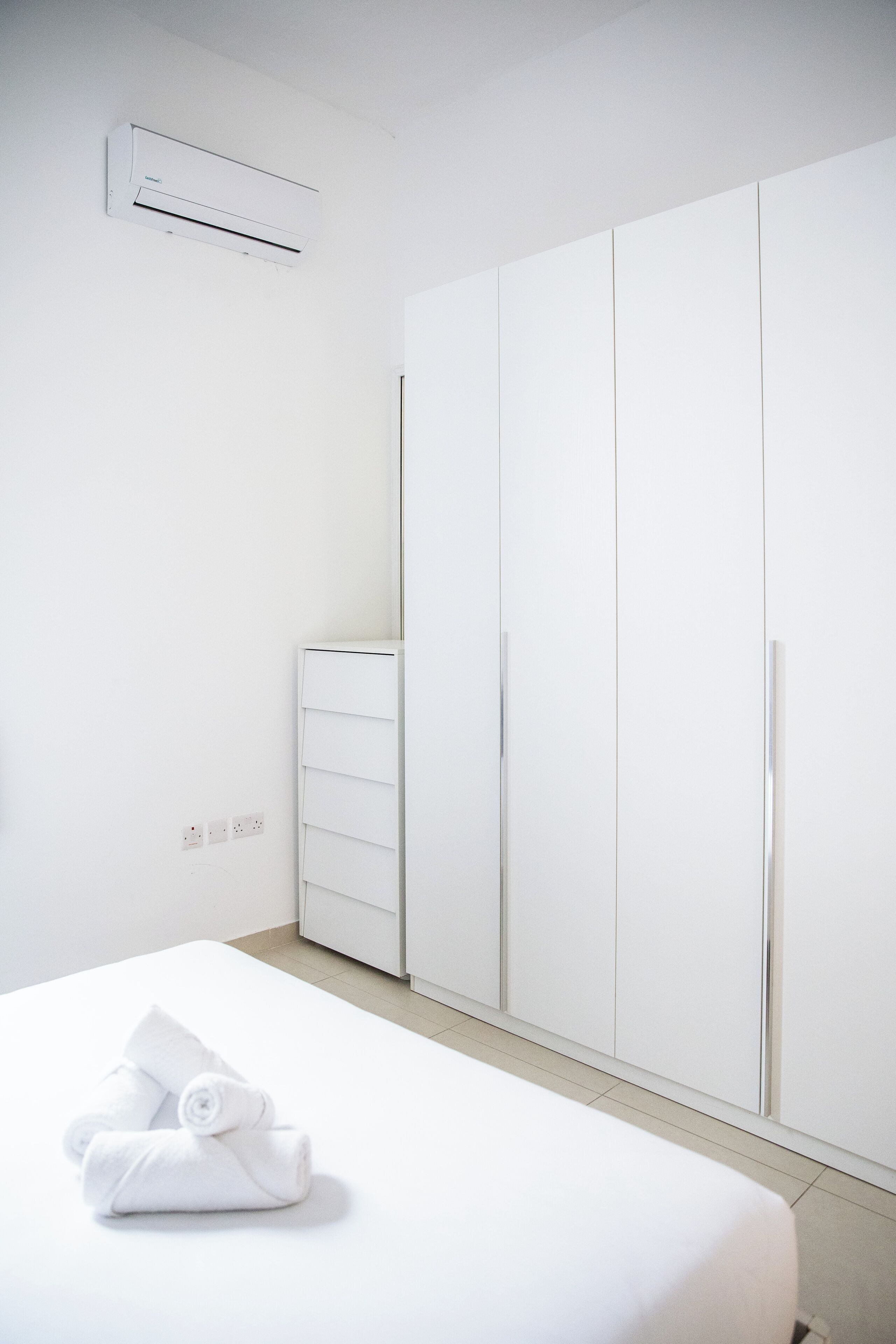 A hotel room with a bed, a wardrobe, a dresser, and an air conditioning unit.