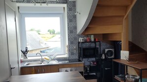 Una cocina moderna con un ventanal grande, armarios de madera, un microondas integrado y una zona de comedor con mesa y sillas.