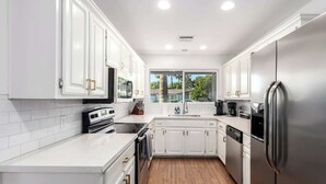 A modern kitchen with white cabinetry, stainless steel appliances, and a wooden floor. - The Desert Bloomhouse | Heated Pool |Sleeps 12 (Scottsdale)