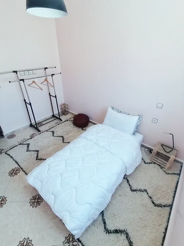 Un dormitorio con cama, perchero, una otomana redonda pequeña y alfombra estampada.