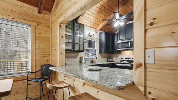 Ein Holzhütten-Interieur mit Küchenbereich, der sich durch Granit-Arbeitsplatten, schwarze Schränke und einen Essbereich mit Holzstühlen auszeichnet.